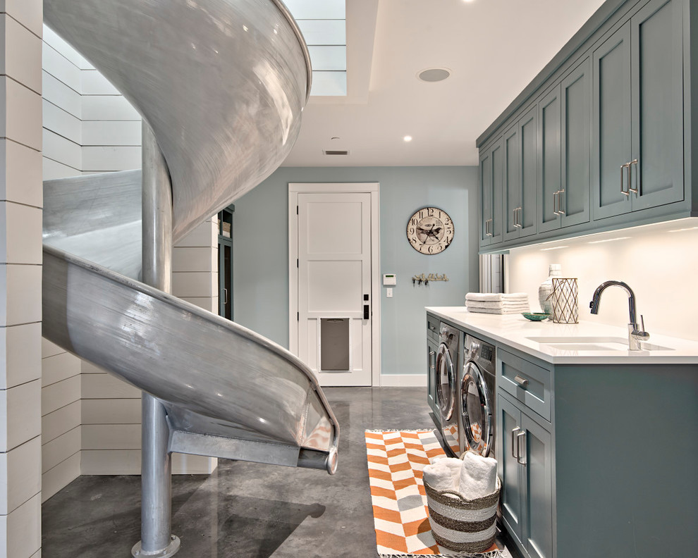 Exempel på en stor lantlig vita linjär vitt tvättstuga enbart för tvätt, med en undermonterad diskho, skåp i shakerstil, betonggolv, en tvättmaskin och torktumlare bredvid varandra, blå skåp, marmorbänkskiva, blå väggar och grått golv