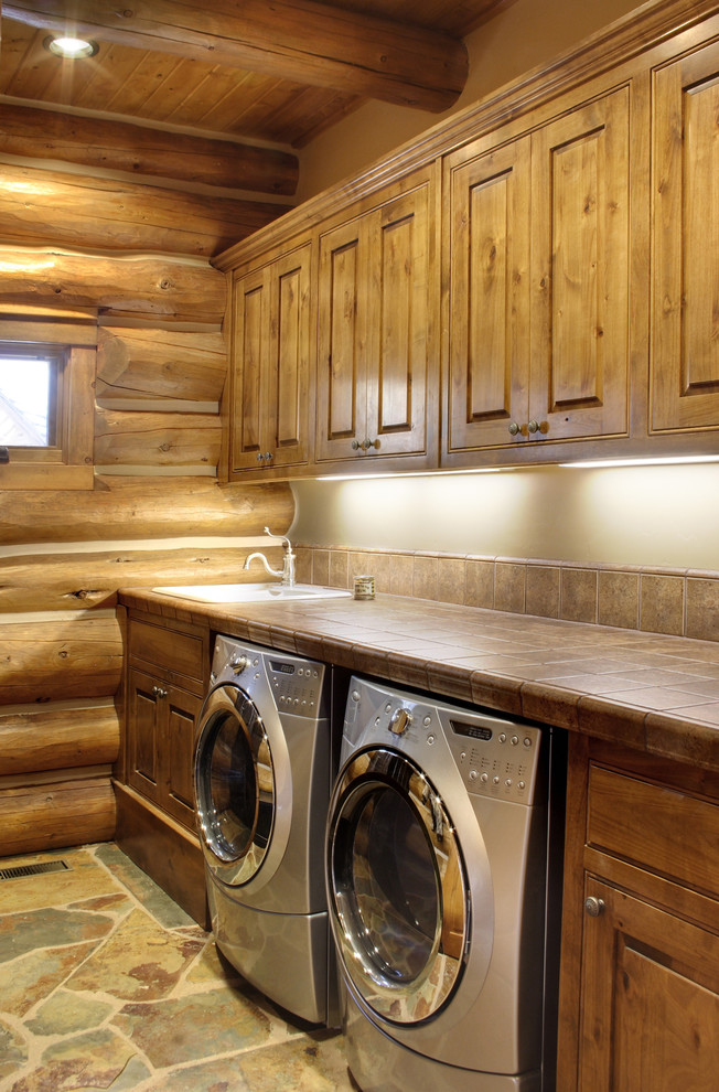 Foto di una sala lavanderia stile rurale di medie dimensioni con lavello da incasso, ante con bugna sagomata, ante in legno bruno, top piastrellato, pareti beige, lavatrice e asciugatrice affiancate, pavimento in ardesia, pavimento beige e top marrone