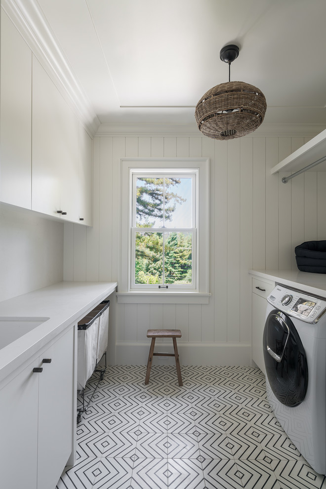 Idéer för stora funkis parallella vitt tvättstugor enbart för tvätt, med en undermonterad diskho, släta luckor, vita skåp, vita väggar, vitt golv, marmorbänkskiva, klinkergolv i keramik och en tvättmaskin och torktumlare bredvid varandra