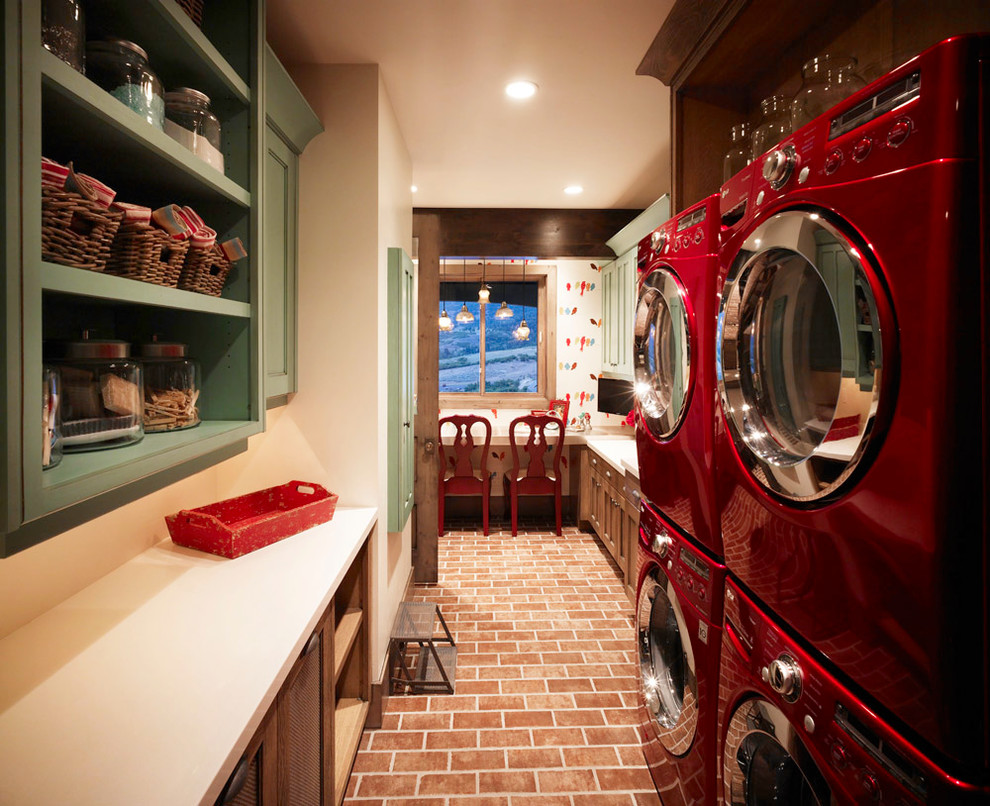 ソルトレイクシティにある高級な中くらいなトラディショナルスタイルのおしゃれな家事室 (ll型、落し込みパネル扉のキャビネット、緑のキャビネット、クオーツストーンカウンター、ベージュの壁、レンガの床、上下配置の洗濯機・乾燥機) の写真