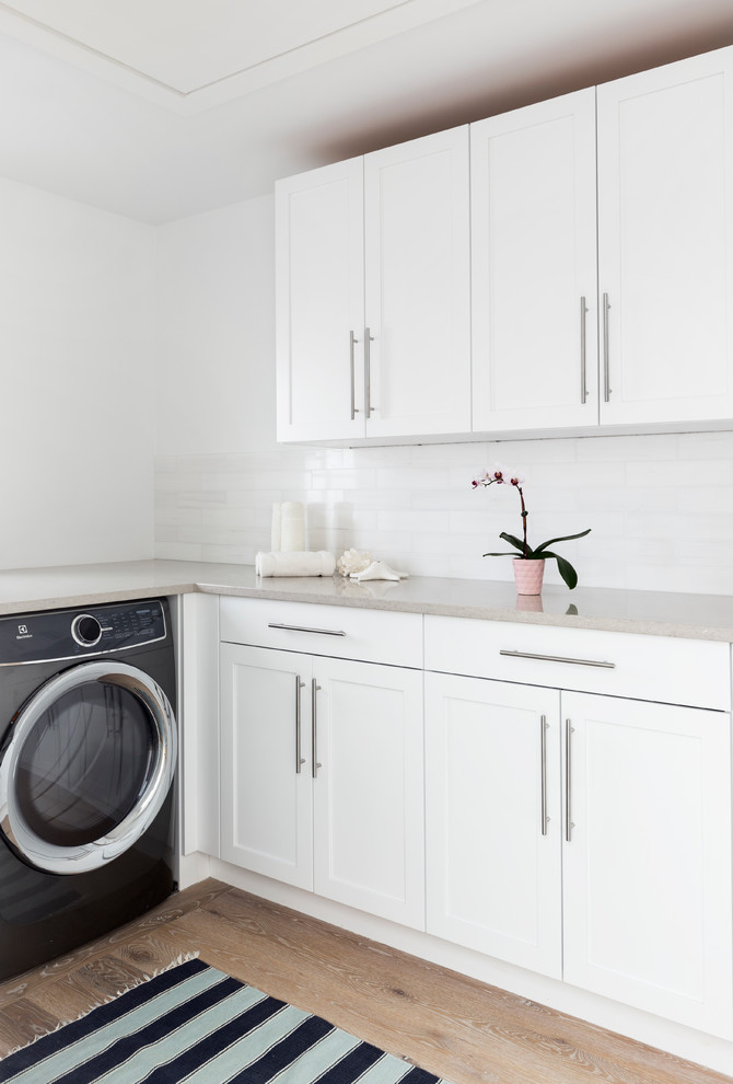 Example of a mid-sized beach style l-shaped light wood floor and beige floor dedicated laundry room design in New York with shaker cabinets, white cabinets, white walls and a side-by-side washer/dryer