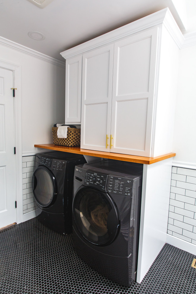 Photo of a medium sized traditional galley utility room in Boston with shaker cabinets, white cabinets, wood worktops, white walls, ceramic flooring, a side by side washer and dryer and black floors.
