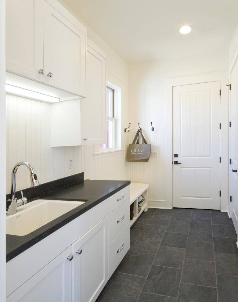 Medium sized farmhouse single-wall utility room in San Francisco with a submerged sink, shaker cabinets, white cabinets, composite countertops, white walls, slate flooring and black worktops.