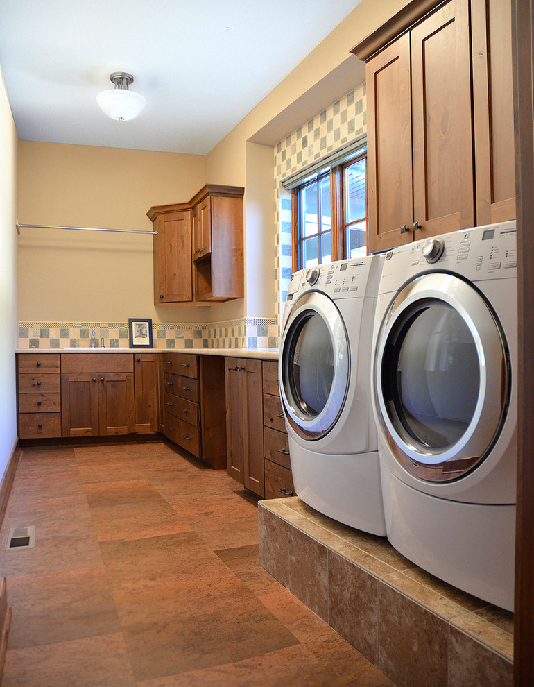 Bild på en stor parallell tvättstuga enbart för tvätt, med en nedsänkt diskho, släta luckor, skåp i mellenmörkt trä, granitbänkskiva, gula väggar, skiffergolv och en tvättmaskin och torktumlare bredvid varandra