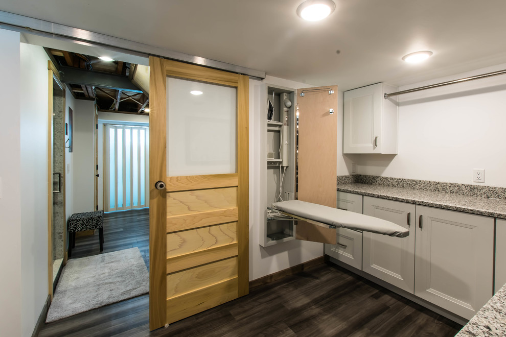 Medium sized rustic l-shaped separated utility room in Other with an utility sink, shaker cabinets, white cabinets, granite worktops, white walls, vinyl flooring, a stacked washer and dryer, grey floors and multicoloured worktops.