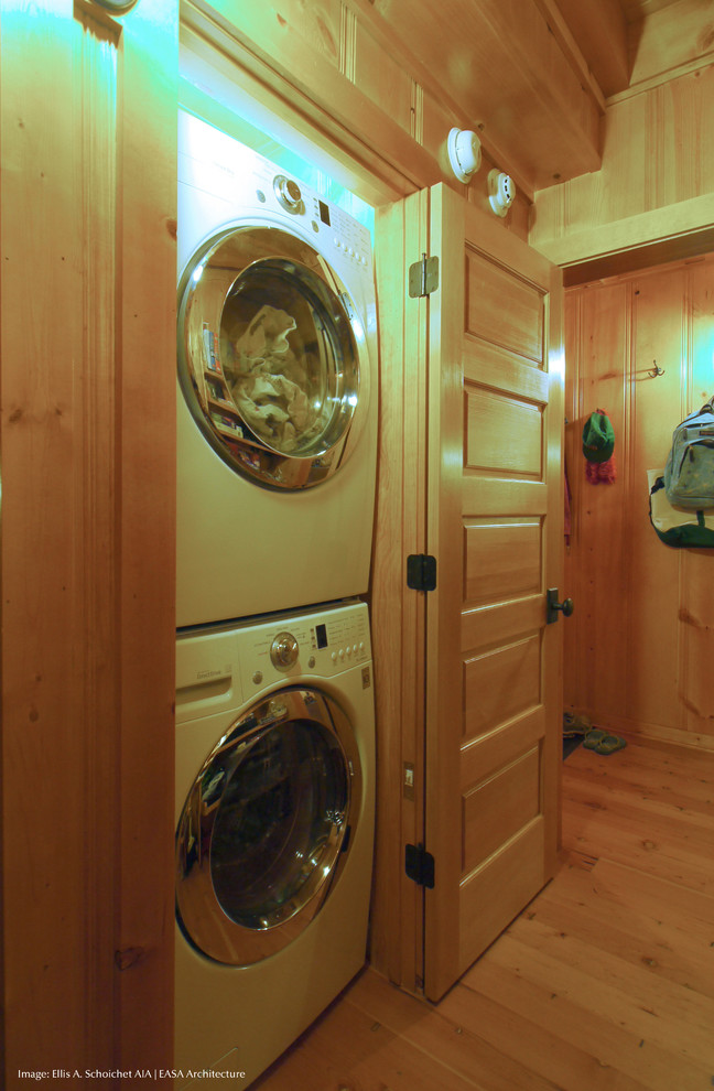 Modelo de armario lavadero rústico pequeño con paredes marrones, suelo de madera clara, lavadora y secadora apiladas y suelo marrón