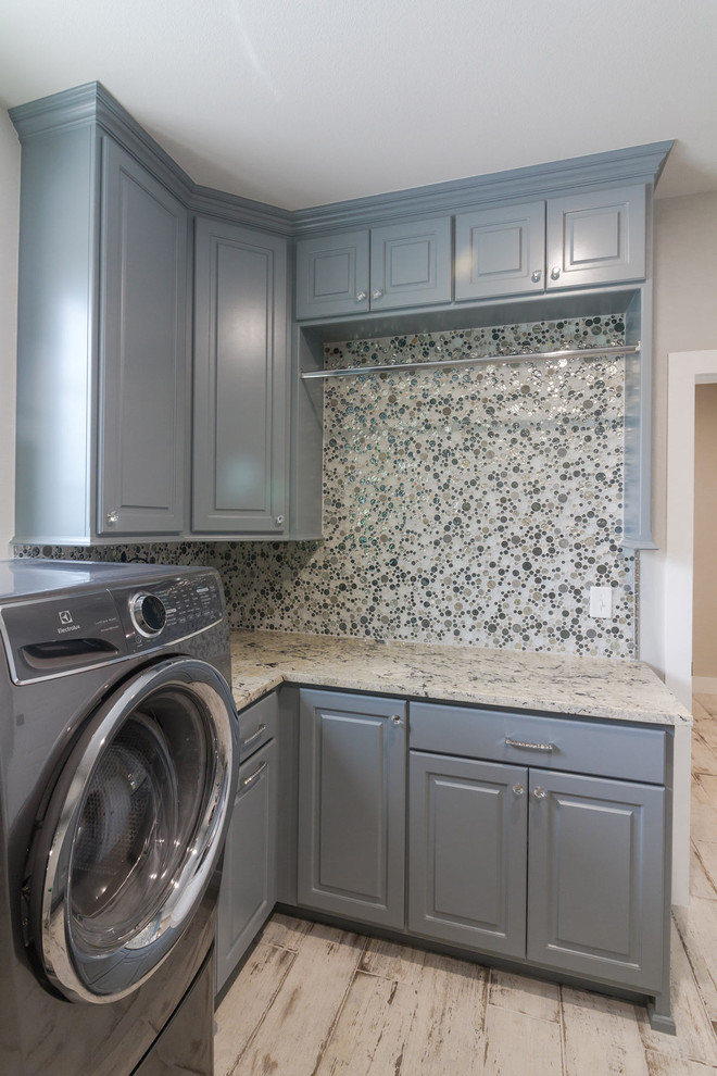 Exempel på ett lantligt grovkök, med blå skåp, granitbänkskiva, grå väggar, klinkergolv i porslin, en tvättmaskin och torktumlare bredvid varandra och grått golv