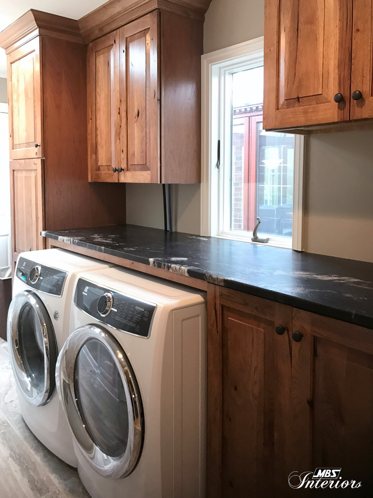 Medium sized rustic single-wall separated utility room in Other with raised-panel cabinets, medium wood cabinets, granite worktops, grey walls, ceramic flooring, a side by side washer and dryer and grey floors.