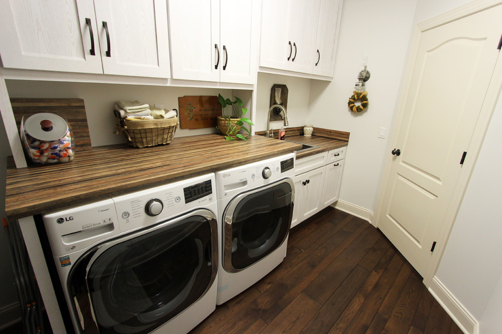Exempel på en mellanstor rustik linjär tvättstuga enbart för tvätt, med en nedsänkt diskho, luckor med infälld panel, vita skåp, laminatbänkskiva, mörkt trägolv, en tvättmaskin och torktumlare bredvid varandra och brunt golv