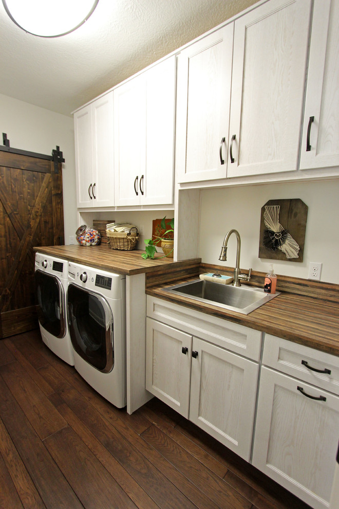 Foto di una sala lavanderia stile rurale di medie dimensioni con lavello da incasso, ante con riquadro incassato, ante bianche, top in laminato, parquet scuro, lavatrice e asciugatrice affiancate e pavimento marrone