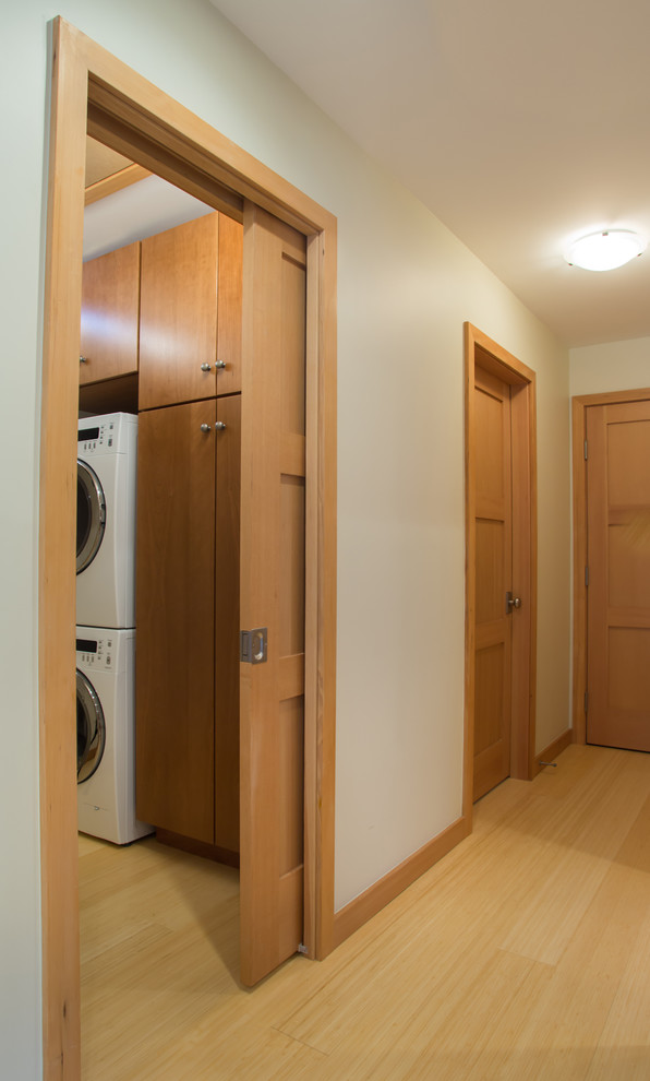 Imagen de lavadero multiusos y lineal campestre pequeño con armarios con paneles lisos, puertas de armario de madera oscura, suelo de bambú, lavadora y secadora apiladas y suelo amarillo