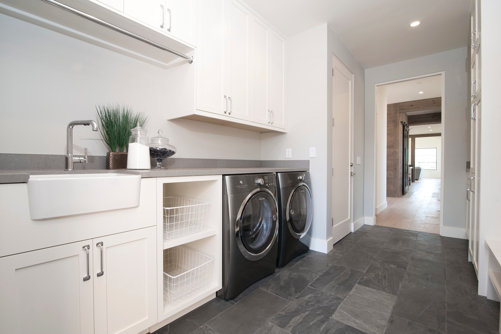 Inspiration for a large farmhouse slate floor dedicated laundry room remodel in San Francisco with a farmhouse sink, shaker cabinets, white cabinets, white walls and a side-by-side washer/dryer