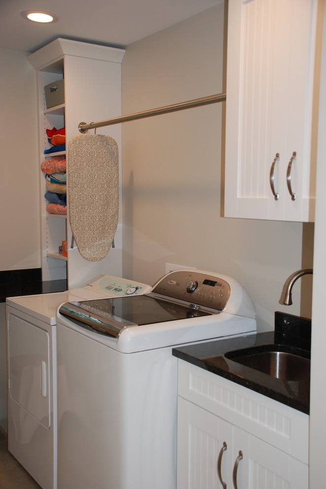 Foto på en mellanstor lantlig l-formad tvättstuga enbart för tvätt, med en undermonterad diskho, öppna hyllor, vita skåp, granitbänkskiva, beige väggar och en tvättmaskin och torktumlare bredvid varandra