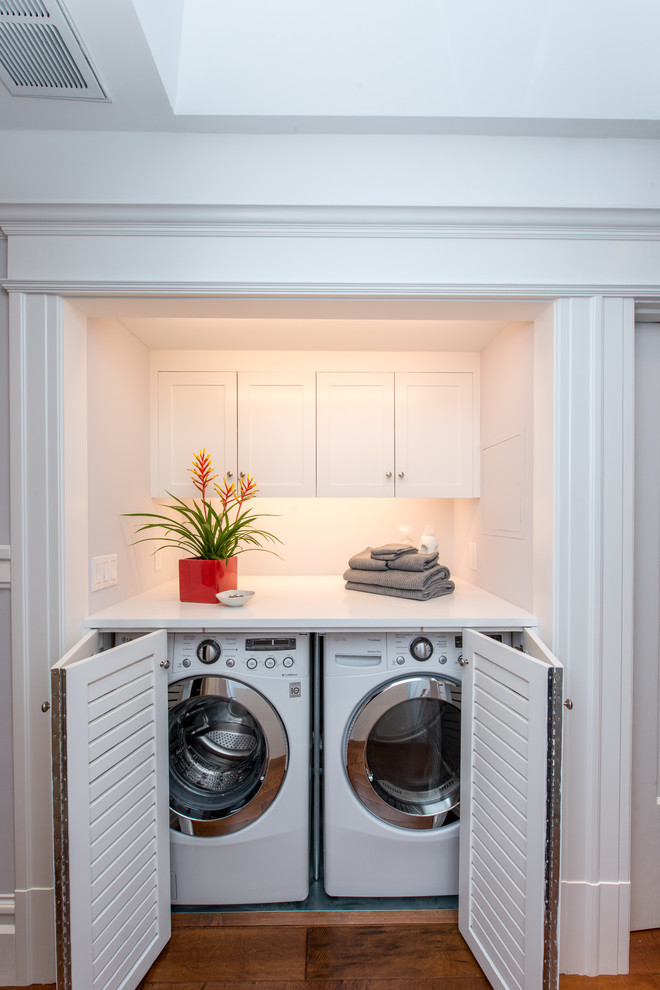 Inredning av en klassisk mellanstor vita linjär vitt liten tvättstuga, med luckor med lamellpanel, vita skåp, blå väggar, en tvättmaskin och torktumlare bredvid varandra och grått golv