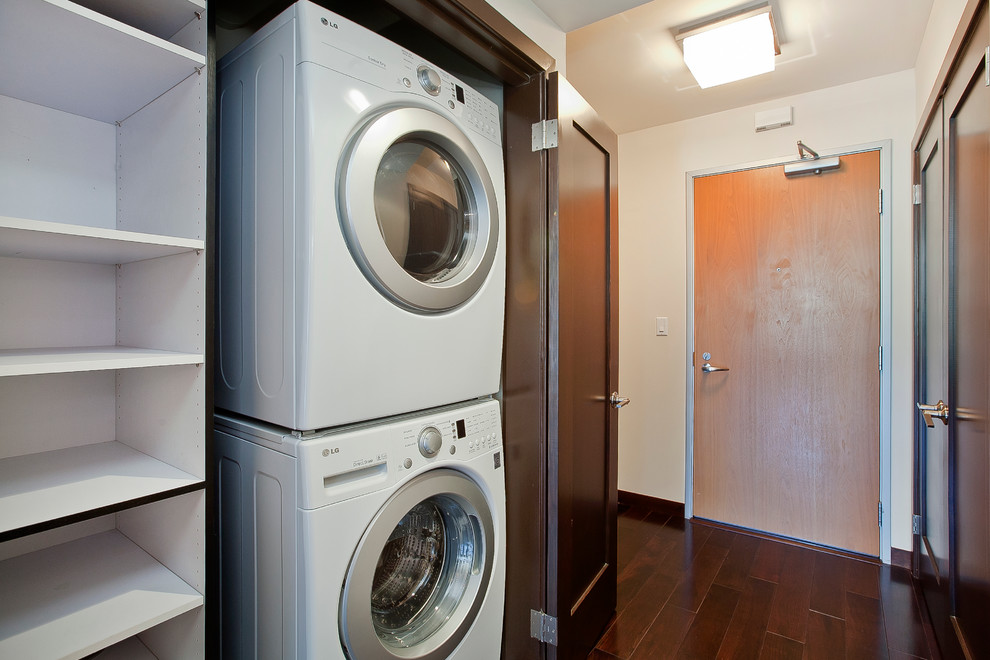 Kleiner Moderner Hauswirtschaftsraum mit Waschmaschinenschrank, dunklem Holzboden und Waschmaschine und Trockner versteckt in San Francisco