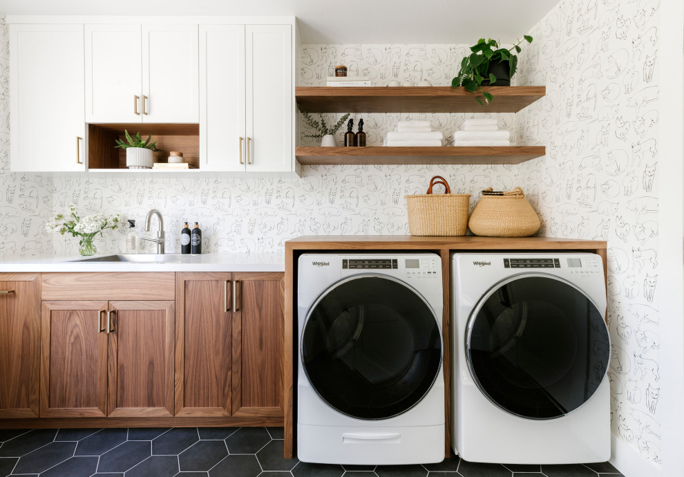 Inspiration pour une buanderie parallèle traditionnelle dédiée et de taille moyenne avec un évier posé, un placard à porte shaker, des portes de placard en bois brun, un plan de travail en quartz modifié, un mur blanc, un sol en carrelage de porcelaine, des machines côte à côte, un sol noir, un plan de travail blanc et du papier peint.