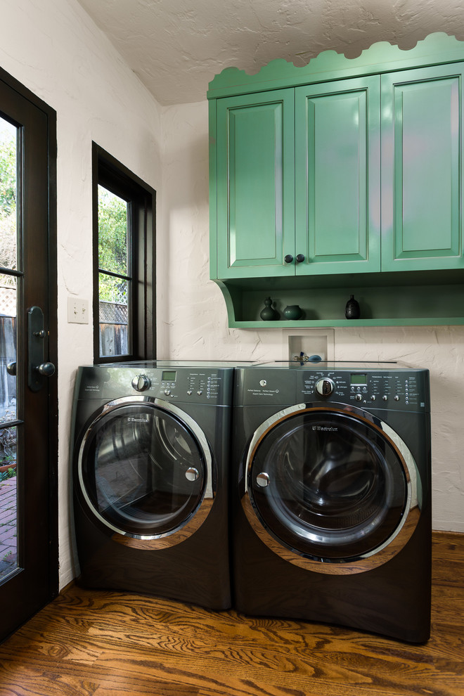 Idéer för medelhavsstil tvättstugor, med luckor med upphöjd panel, gröna skåp, vita väggar, mörkt trägolv och en tvättmaskin och torktumlare bredvid varandra