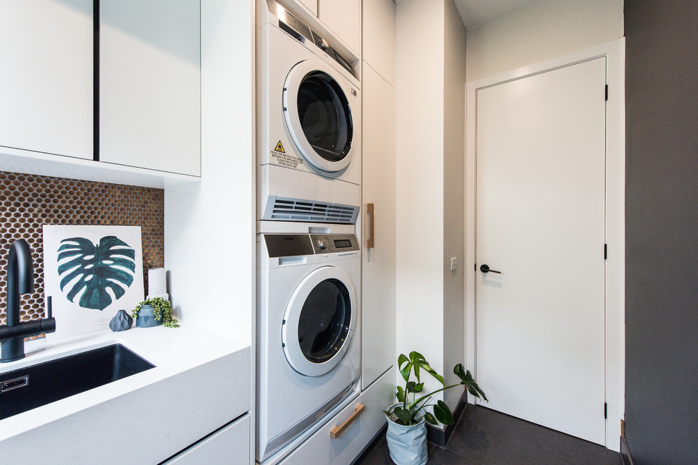 メルボルンにある中くらいなコンテンポラリースタイルのおしゃれな洗濯室 (I型、アンダーカウンターシンク、フラットパネル扉のキャビネット、白いキャビネット、クオーツストーンカウンター、黒い壁、上下配置の洗濯機・乾燥機) の写真