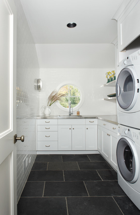 Exempel på en lantlig tvättstuga, med en undermonterad diskho, skåp i shakerstil, vita skåp, bänkskiva i rostfritt stål, vita väggar, skiffergolv och en tvättpelare