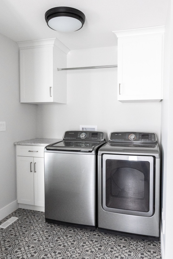 Imagen de cuarto de lavado lineal campestre de tamaño medio con armarios estilo shaker, puertas de armario blancas, paredes blancas, lavadora y secadora juntas y suelo multicolor