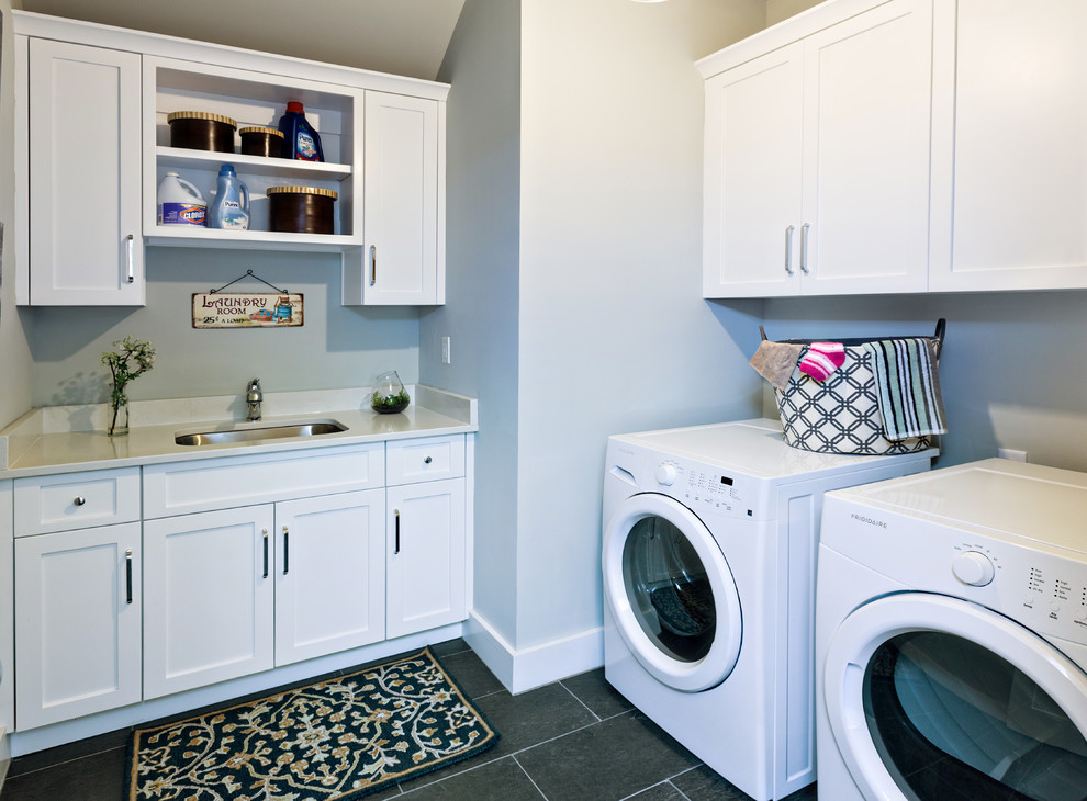 Exempel på en mellanstor lantlig tvättstuga enbart för tvätt, med en undermonterad diskho, skåp i shakerstil, vita skåp, bänkskiva i kvarts, blå väggar, skiffergolv och en tvättmaskin och torktumlare bredvid varandra