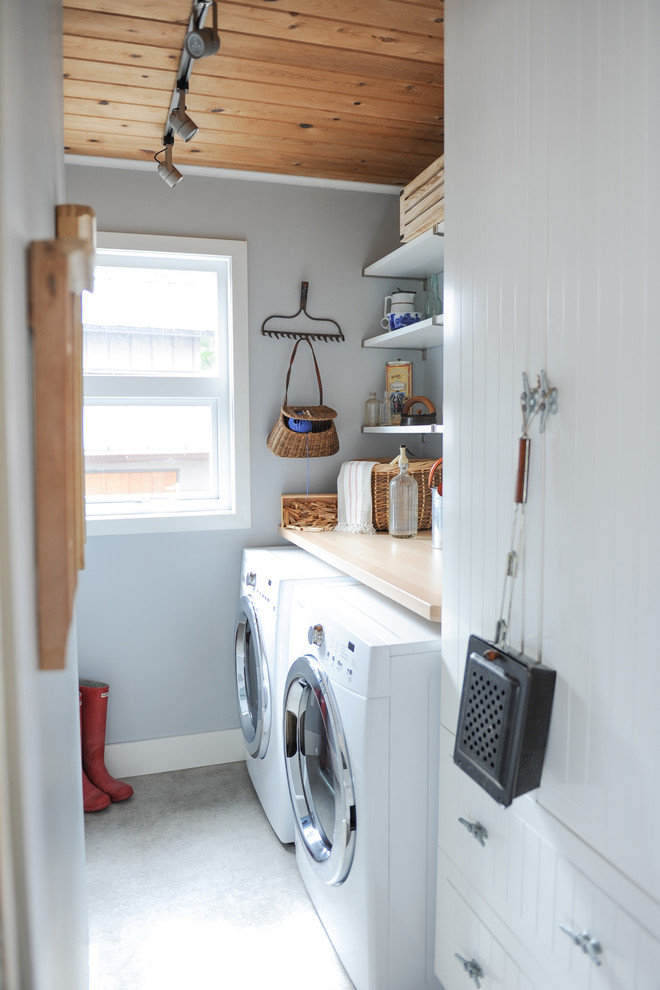 Immagine di una sala lavanderia stile rurale di medie dimensioni con ante bianche, top in legno, pareti grigie, pavimento in cemento, lavatrice e asciugatrice affiancate e ante lisce