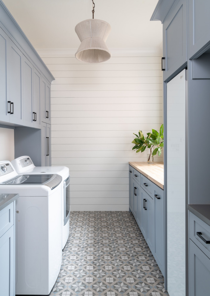 Inspiration för stora klassiska parallella beige tvättstugor enbart för tvätt, med skåp i shakerstil, blå skåp, träbänkskiva, vita väggar, klinkergolv i porslin, en tvättmaskin och torktumlare bredvid varandra och grått golv