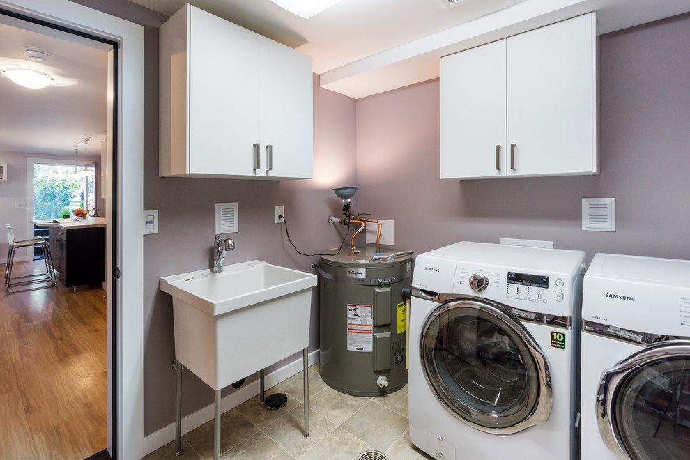 Exempel på en liten modern parallell tvättstuga enbart för tvätt, med en allbänk, släta luckor, vita skåp, lila väggar, klinkergolv i keramik, en tvättmaskin och torktumlare bredvid varandra och beiget golv