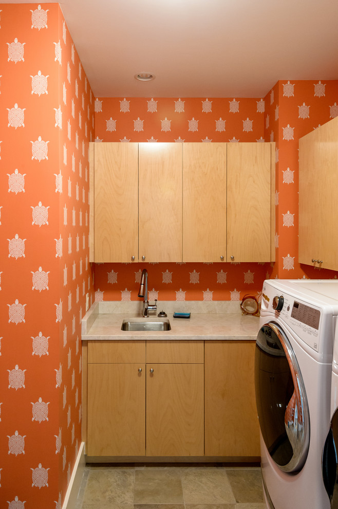 Bild på en mellanstor funkis parallell tvättstuga enbart för tvätt, med en undermonterad diskho, släta luckor, skåp i ljust trä, bänkskiva i kvartsit, orange väggar, skiffergolv, en tvättmaskin och torktumlare bredvid varandra och beiget golv