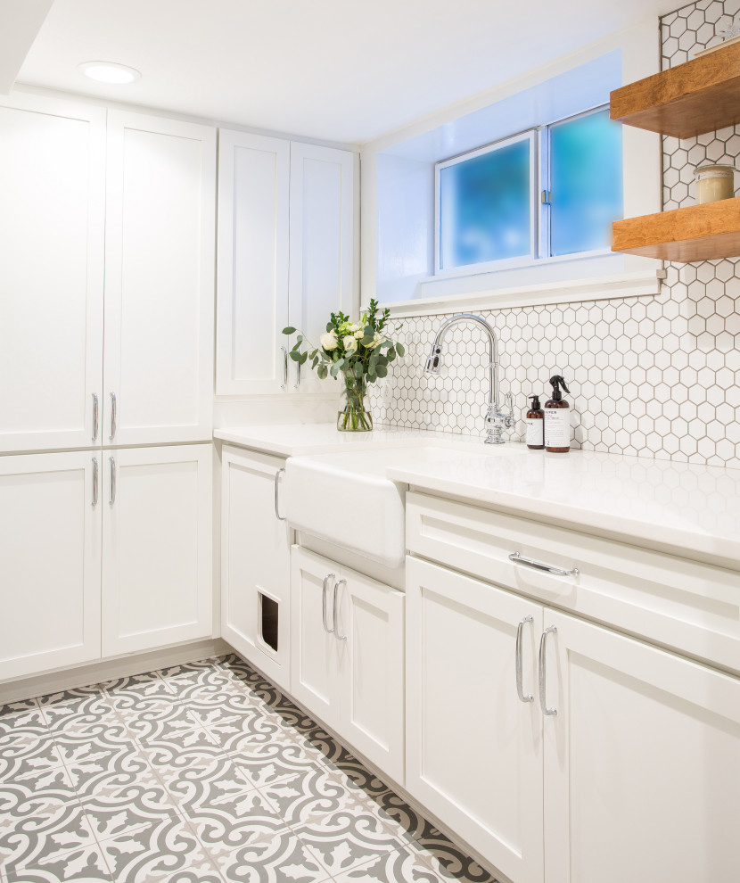 Ejemplo de cuarto de lavado campestre, de tamaño medio, con fregadero sobremueble, armarios estilo shaker, puertas de armario blancas, encimera de cuarzo compacto, paredes blancas, suelo de baldosas de porcelana, lavadora y secadora apiladas, encimeras blancas y suelo gris