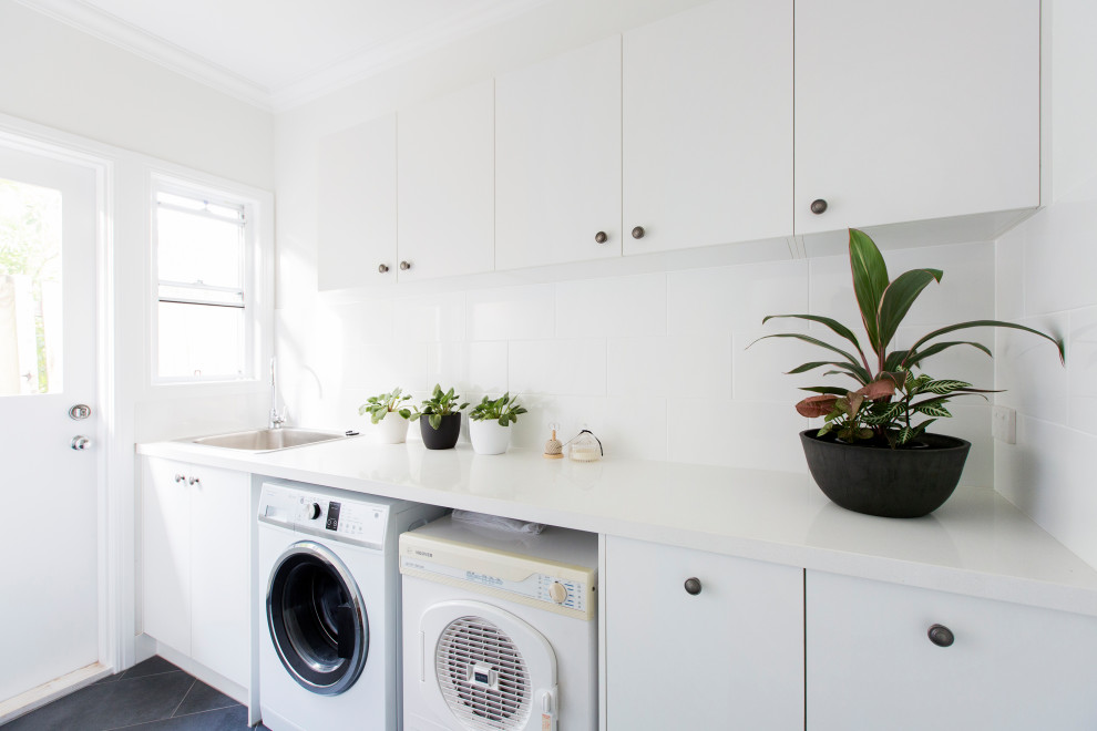 Idéer för att renovera en mellanstor vintage vita parallell vitt tvättstuga enbart för tvätt, med en nedsänkt diskho, släta luckor, vita skåp, bänkskiva i kvartsit, vita väggar, klinkergolv i keramik, en tvättmaskin och torktumlare bredvid varandra och grått golv