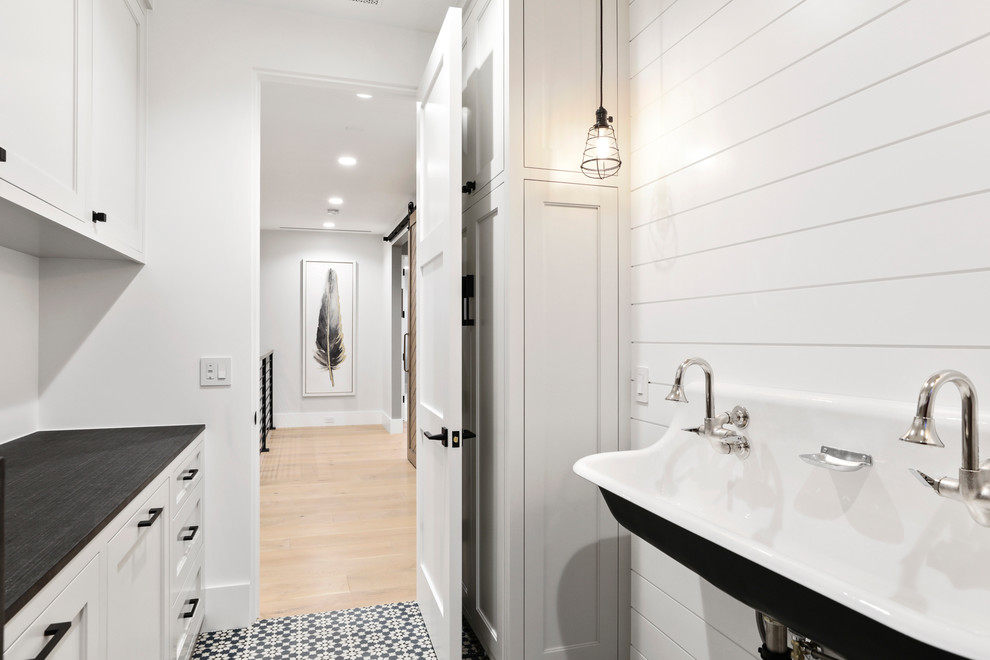 Exempel på en liten modern parallell tvättstuga enbart för tvätt, med en allbänk, luckor med infälld panel, vita skåp, vita väggar, betonggolv, en tvättmaskin och torktumlare bredvid varandra och blått golv