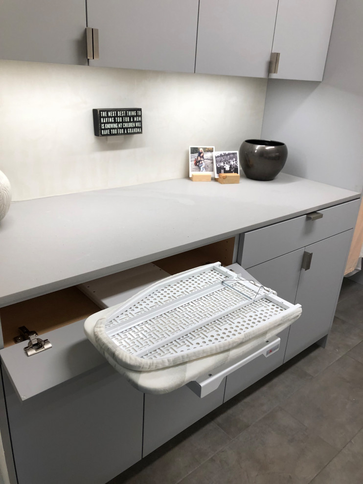 Modelo de cuarto de lavado de galera contemporáneo de tamaño medio con fregadero bajoencimera, armarios con paneles lisos, puertas de armario grises, paredes beige, lavadora y secadora juntas, suelo gris y encimeras grises