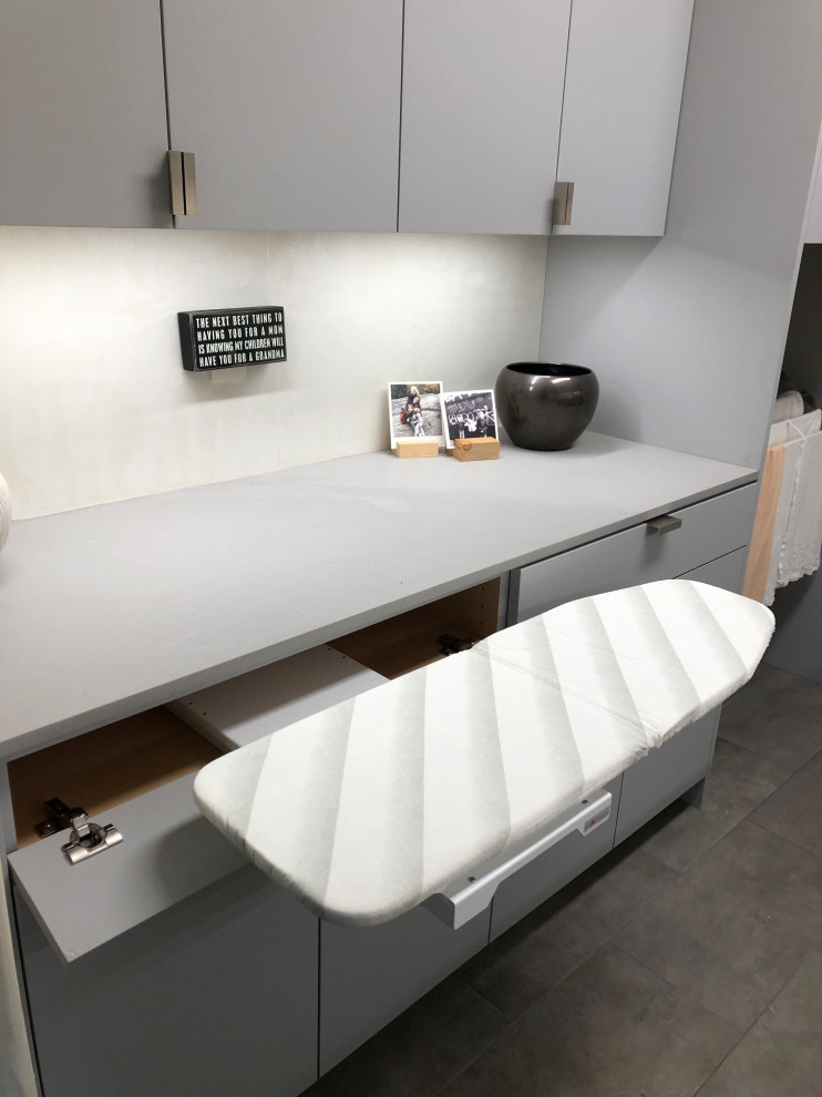Immagine di una sala lavanderia design di medie dimensioni con lavello sottopiano, ante lisce, ante grigie, pareti beige, lavatrice e asciugatrice affiancate, pavimento grigio e top grigio
