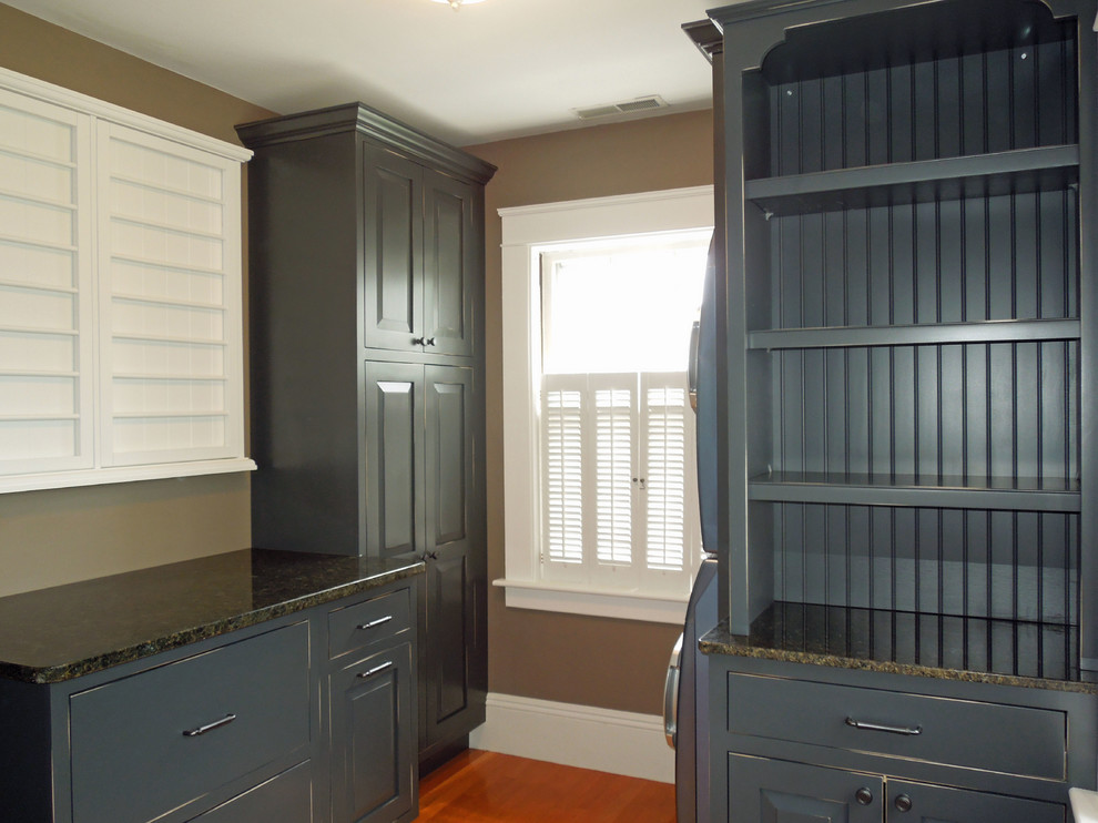 Zweizeilige, Mittelgroße Klassische Waschküche mit profilierten Schrankfronten, grauen Schränken, Granit-Arbeitsplatte, braunem Holzboden und Waschmaschine und Trockner gestapelt in Charleston