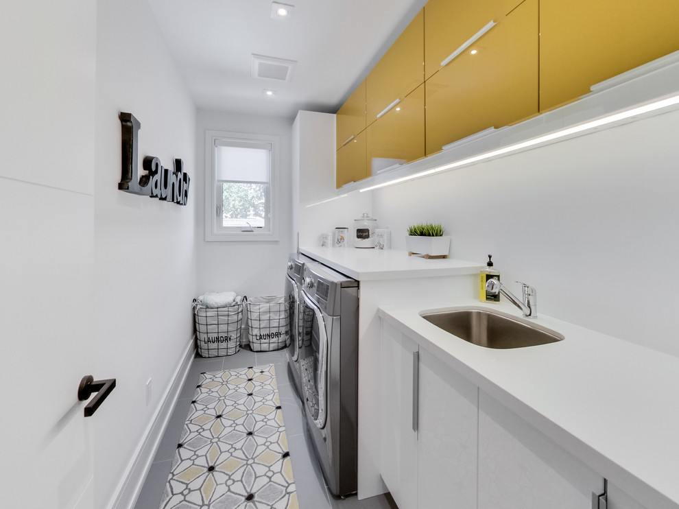 Einzeiliger Moderner Hauswirtschaftsraum mit Unterbauwaschbecken, flächenbündigen Schrankfronten, gelben Schränken, weißer Wandfarbe, Waschmaschine und Trockner nebeneinander und weißer Arbeitsplatte in Toronto