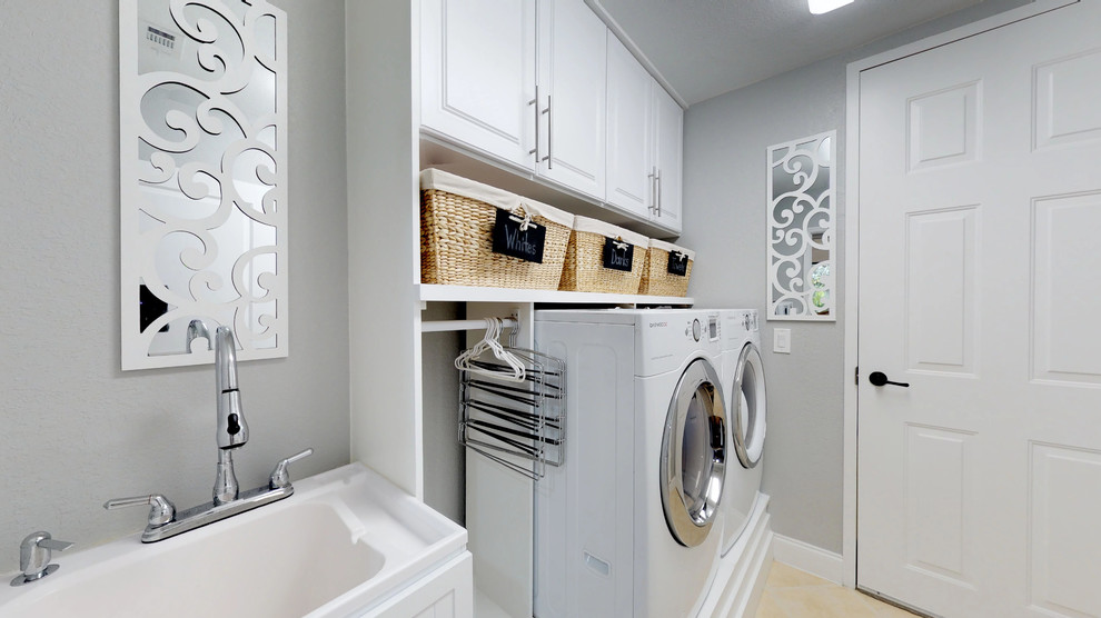 Foto på en maritim tvättstuga enbart för tvätt, med en allbänk, skåp i shakerstil, vita skåp, grå väggar och en tvättmaskin och torktumlare bredvid varandra