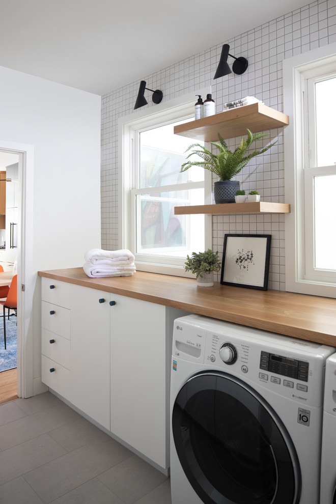 Idéer för att renovera en funkis bruna brunt tvättstuga enbart för tvätt, med släta luckor, vita skåp, träbänkskiva, vita väggar, en tvättmaskin och torktumlare bredvid varandra och grått golv