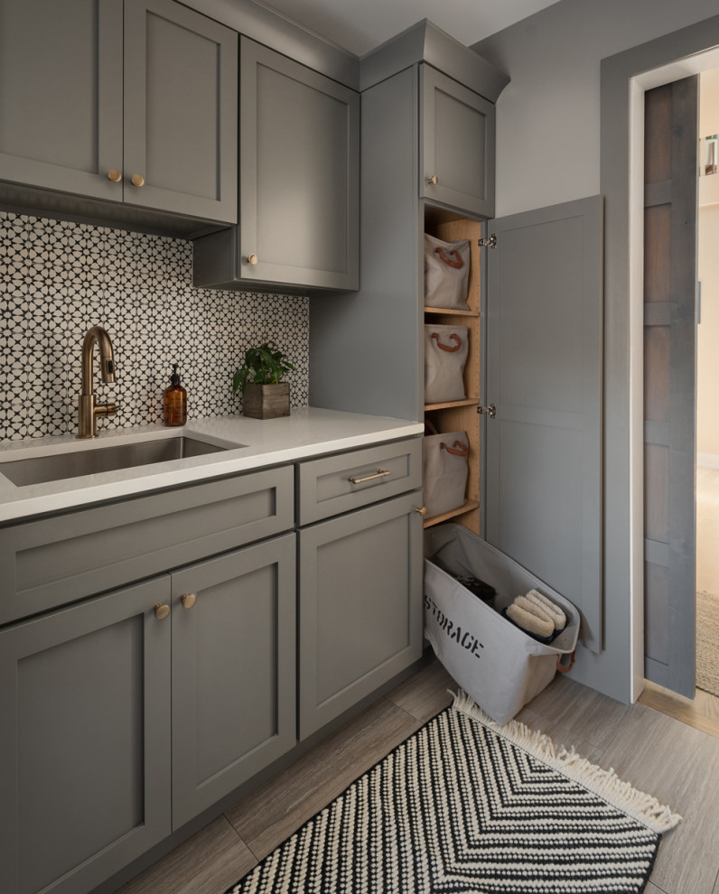 Diseño de lavadero multiusos y lineal, clásico renovado, de tamaño medio, con fregadero bajoencimera, armarios estilo shaker, puertas de armario grises, encimera de cuarzo compacto, salpicadero multicolor, salpicadero de azulejos de cemento, paredes grises, suelo de baldosas de porcelana, lavadora y secadora juntas, suelo gris y encimeras blancas