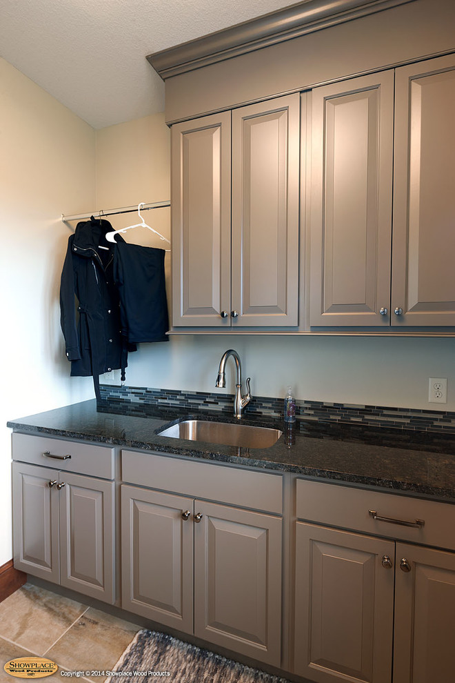 This is an example of a traditional utility room in Other with raised-panel cabinets and a stacked washer and dryer.