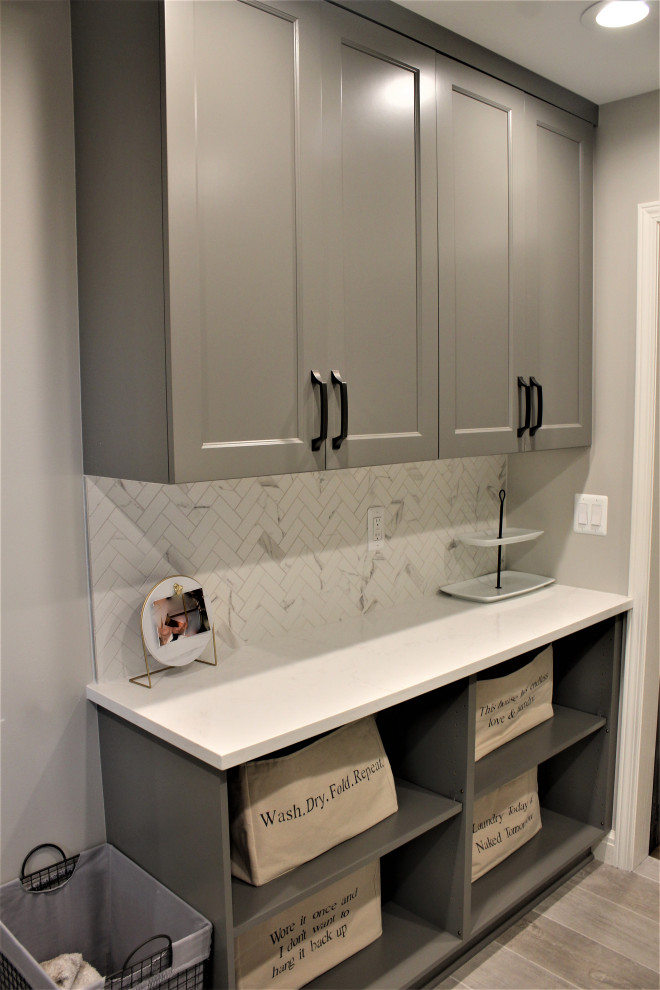 Inspiration for a large classic u-shaped utility room in Detroit with a submerged sink, flat-panel cabinets, grey cabinets, engineered stone countertops, grey splashback, stone tiled splashback, grey walls, porcelain flooring, a side by side washer and dryer, grey floors and white worktops.