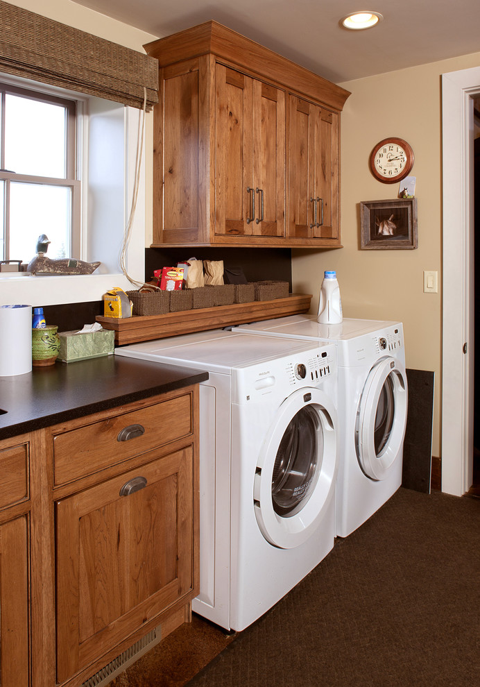 Esempio di una sala lavanderia stile rurale di medie dimensioni con lavello sottopiano, ante in stile shaker, ante in legno bruno, top in granito, pareti beige, pavimento in laminato, lavatrice e asciugatrice affiancate, pavimento marrone e top nero