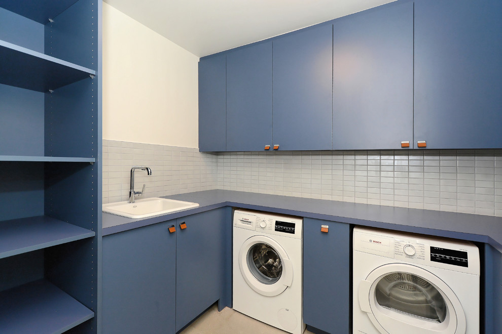 Foto di una sala lavanderia minimalista di medie dimensioni con lavello da incasso, ante lisce, ante blu, top in laminato, pareti bianche, pavimento in cemento, lavatrice e asciugatrice affiancate, pavimento beige e top blu