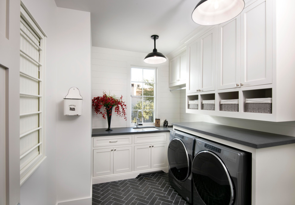 Inredning av en klassisk svarta svart tvättstuga, med en dubbel diskho, skåp i shakerstil, vita skåp, vita väggar, en tvättmaskin och torktumlare bredvid varandra och svart golv