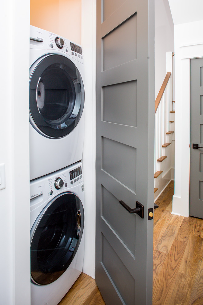 Immagine di un piccolo ripostiglio-lavanderia moderno con pavimento in legno massello medio e lavatrice e asciugatrice a colonna