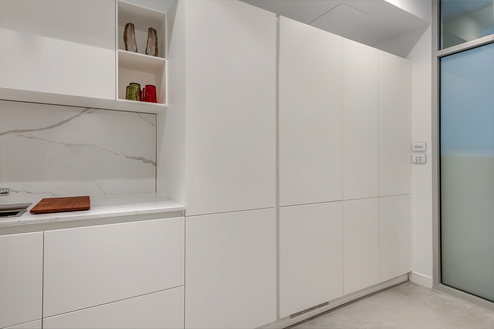 Foto di una piccola lavanderia multiuso moderna con ante bianche, top in quarzo composito, pareti bianche, pavimento con piastrelle in ceramica, lavatrice e asciugatrice nascoste e ante lisce