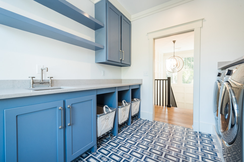 Foto på en stor funkis parallell tvättstuga enbart för tvätt, med en undermonterad diskho, skåp i shakerstil, blå skåp, bänkskiva i kvarts, vita väggar, en tvättmaskin och torktumlare bredvid varandra och flerfärgat golv