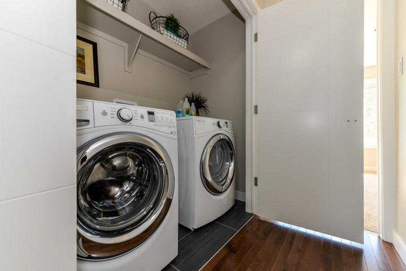 Bild på en liten tvättstuga, med grå väggar och en tvättmaskin och torktumlare bredvid varandra
