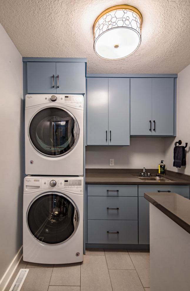 Dedicated laundry room - small modern single-wall porcelain tile and gray floor dedicated laundry room idea in Other with an undermount sink, flat-panel cabinets, blue cabinets, quartz countertops, beige walls, a stacked washer/dryer and gray countertops