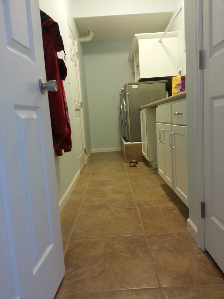 Photo of a traditional utility room in Other with flat-panel cabinets, white cabinets, laminate countertops, green walls, porcelain flooring, a side by side washer and dryer and beige floors.
